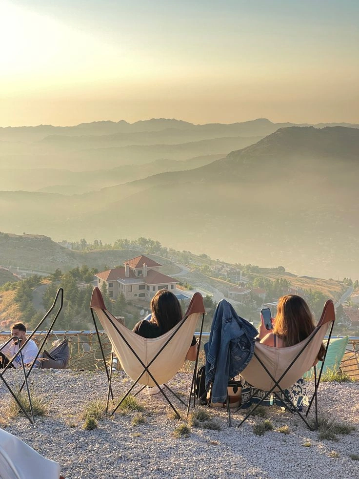 Two women sit on outdoor lounge chairs facing a scenic mountain view in Zaarour, Lebanon